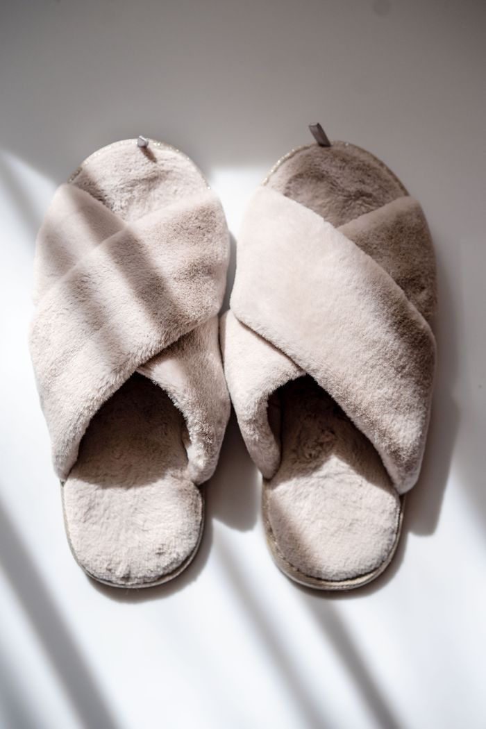 A pair of stylish fluffy beige slippers casting shadows on a sunlit floor.