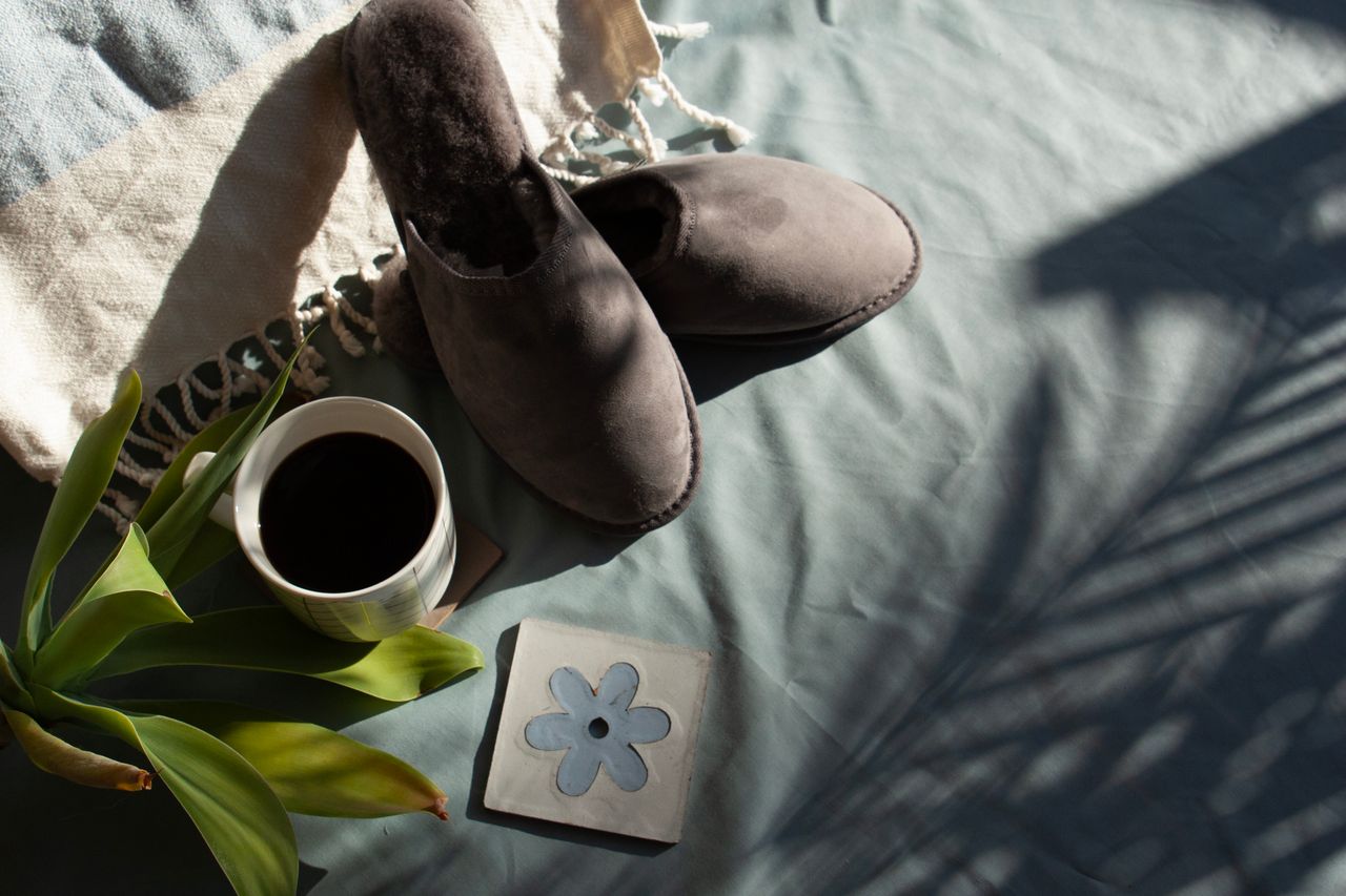 A relaxing morning setup with gray slippers, coffee, and greenery in soft light.